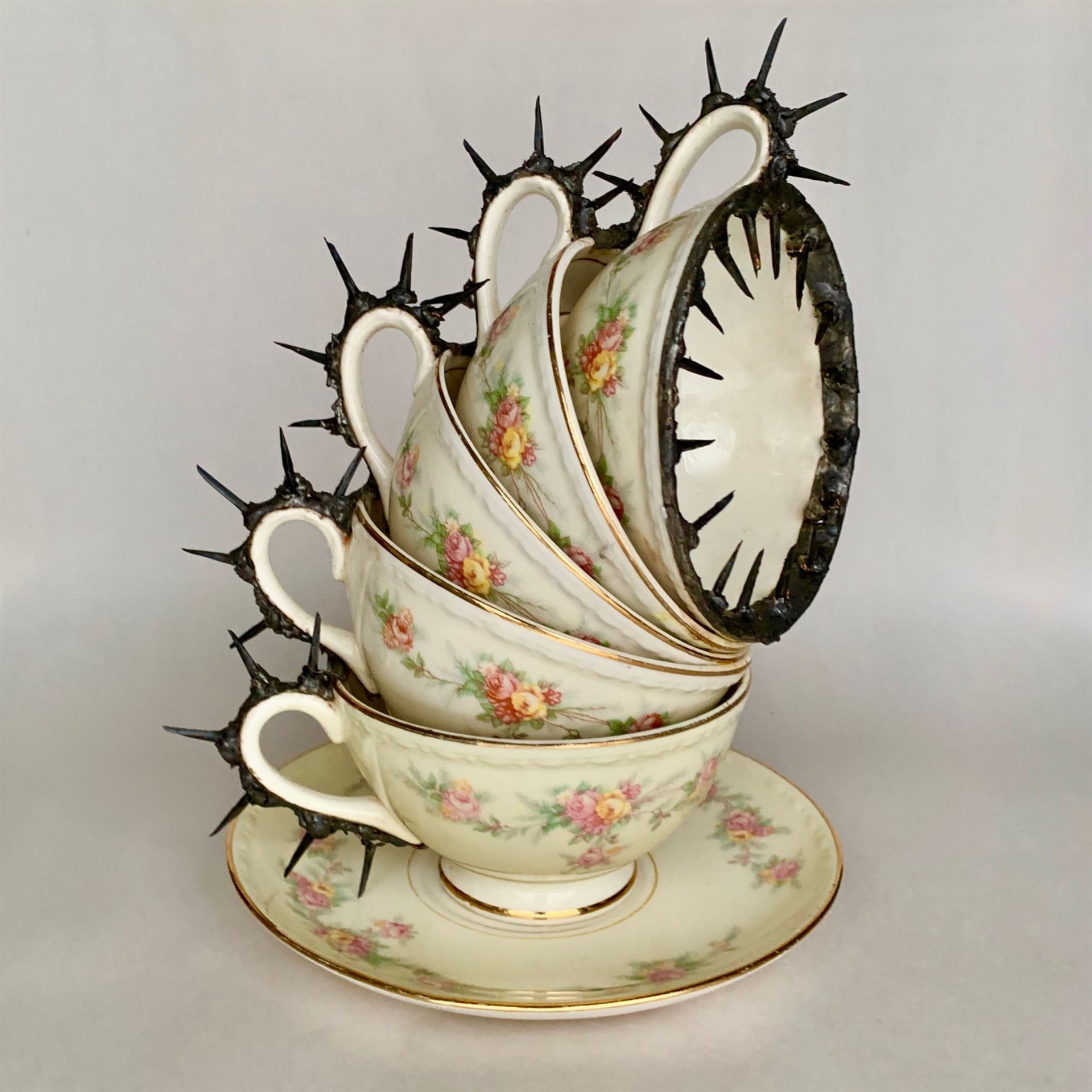 A photo of a sculpture of stacked teacups and saucer lined with barbed wire