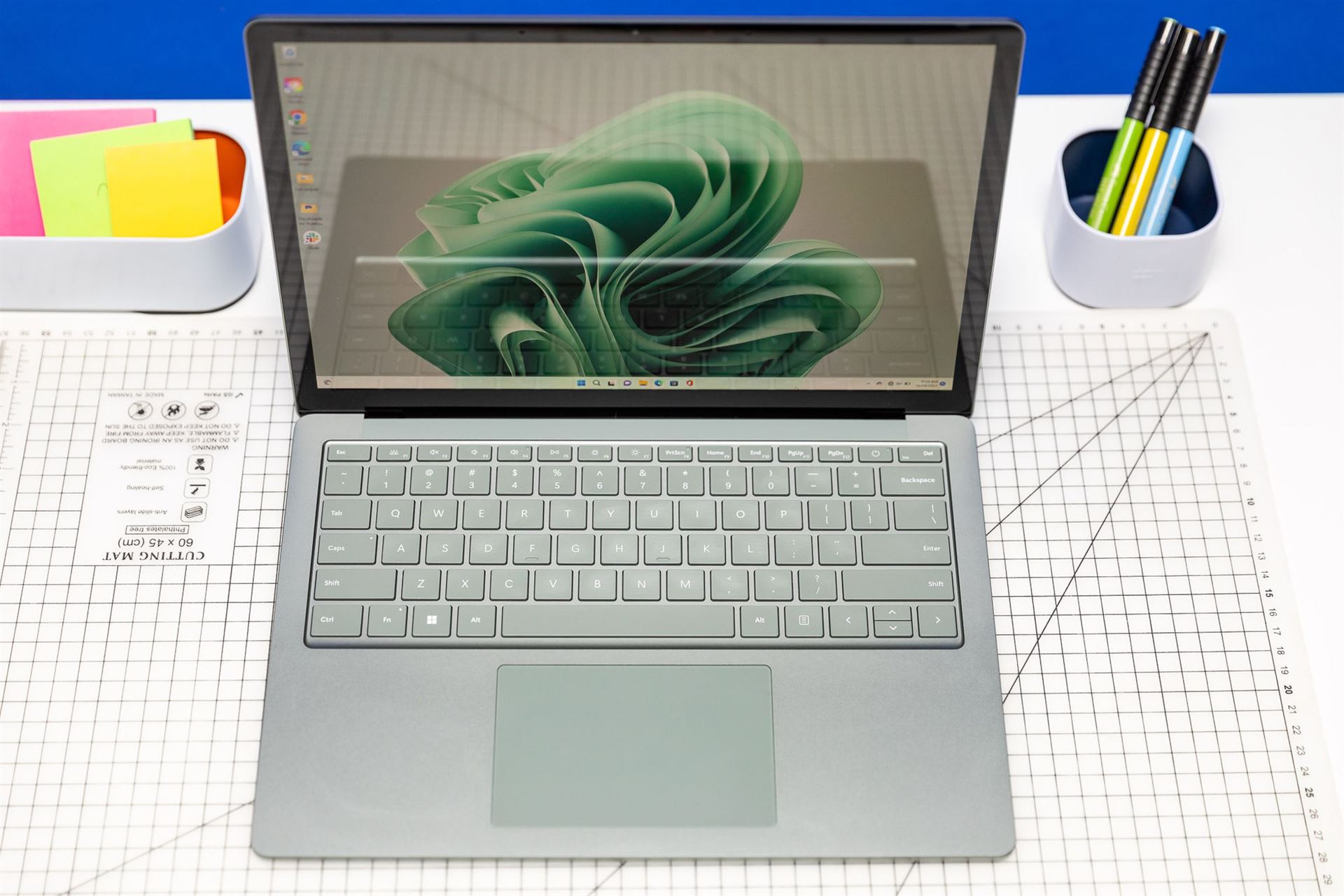 The Surface Laptop 5 seen from above, open, on a desk with Post-its and pencils. The screen displays a green ribbon.