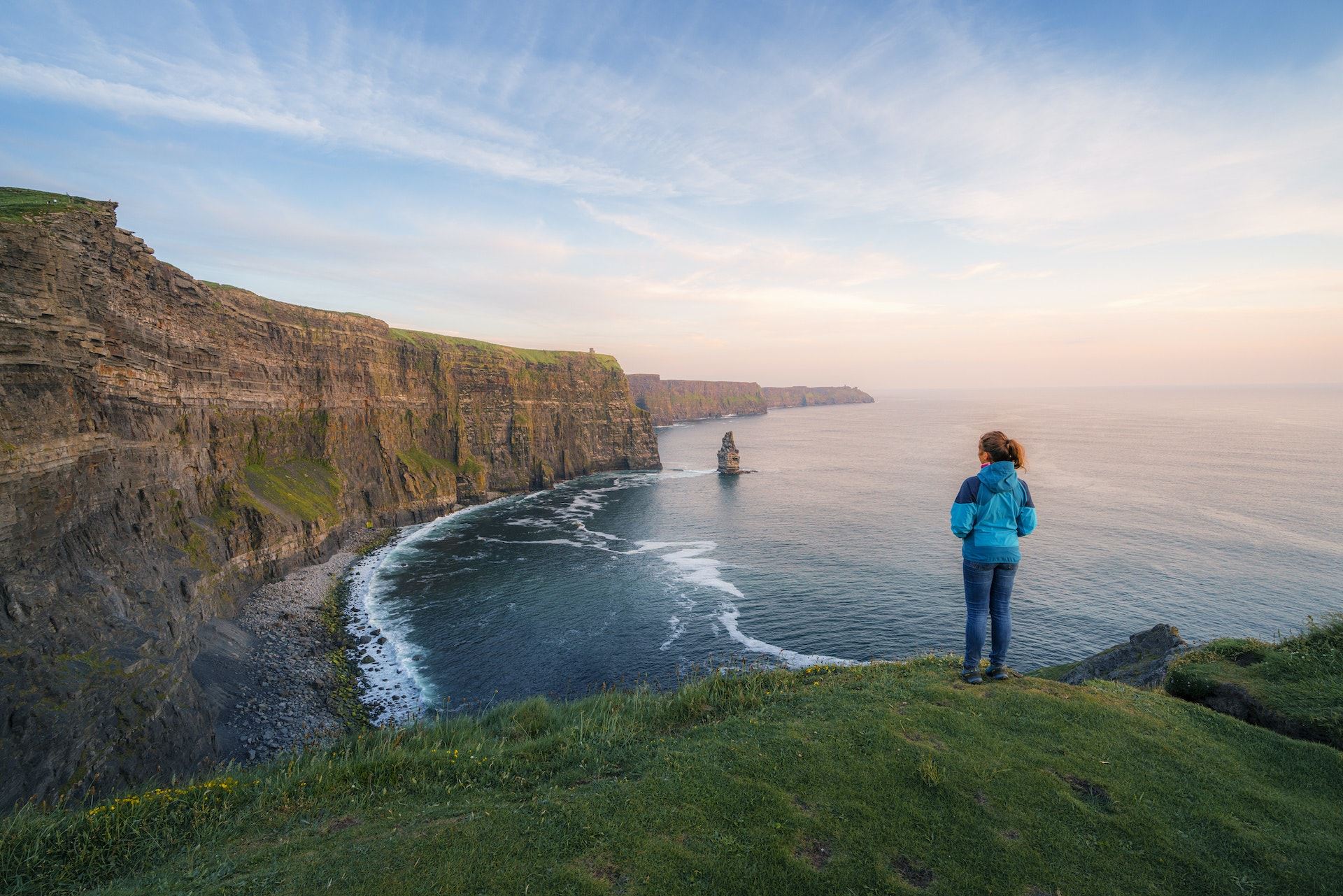 Ireland, County Clare, Lahinch: tourist gazing at the majestic Cliffs of Moher at sunset in late spring.
