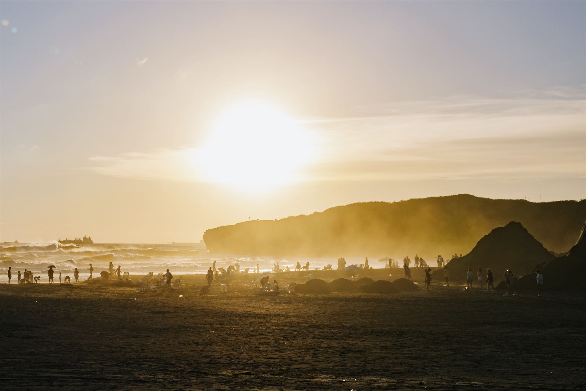 Crowds on the beach are silhouetted as the sun sets, streaking orange across the sky