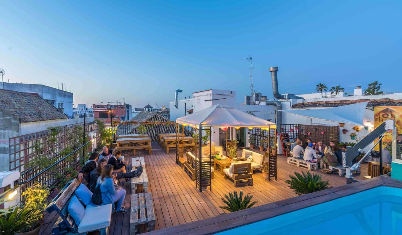 People lounging on a large rooftop terrace with the corner of a pool in the foreground and the cityscape of Sevilla, Spain in the background
